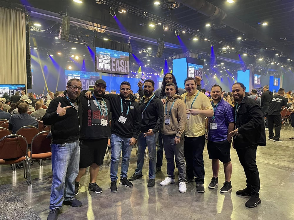 Conference attendees networking at Hozio event with stage and large screens foregrounded.