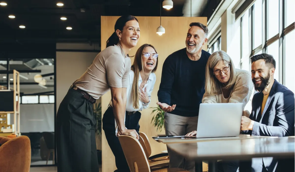 Joyful business team collaborating around a laptop in a modern office environment.