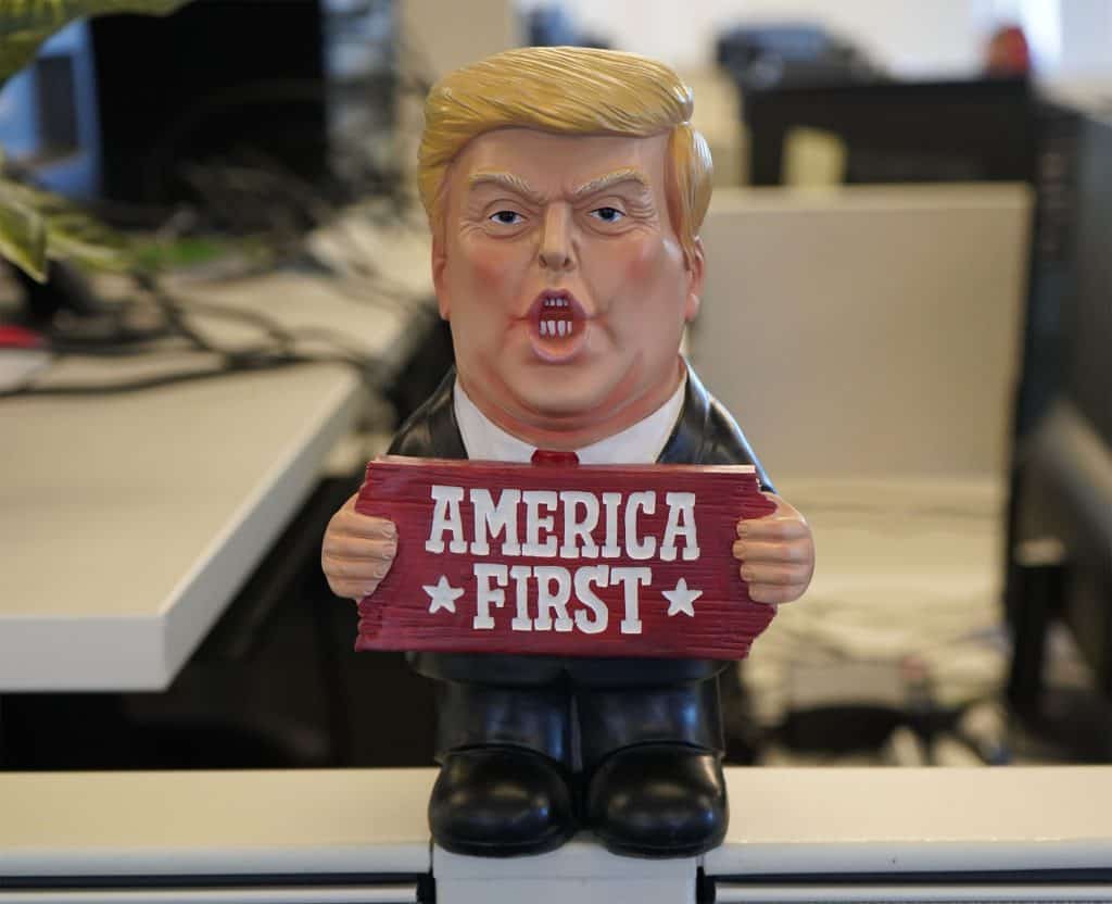 Donald Trump bobblehead holding a "America First" sign, placed on an office desk.