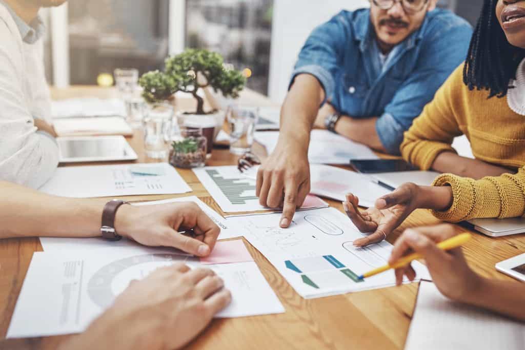 Professional team discussing business strategy at a wooden table with charts and graphs, representing collaboration and data analysis.